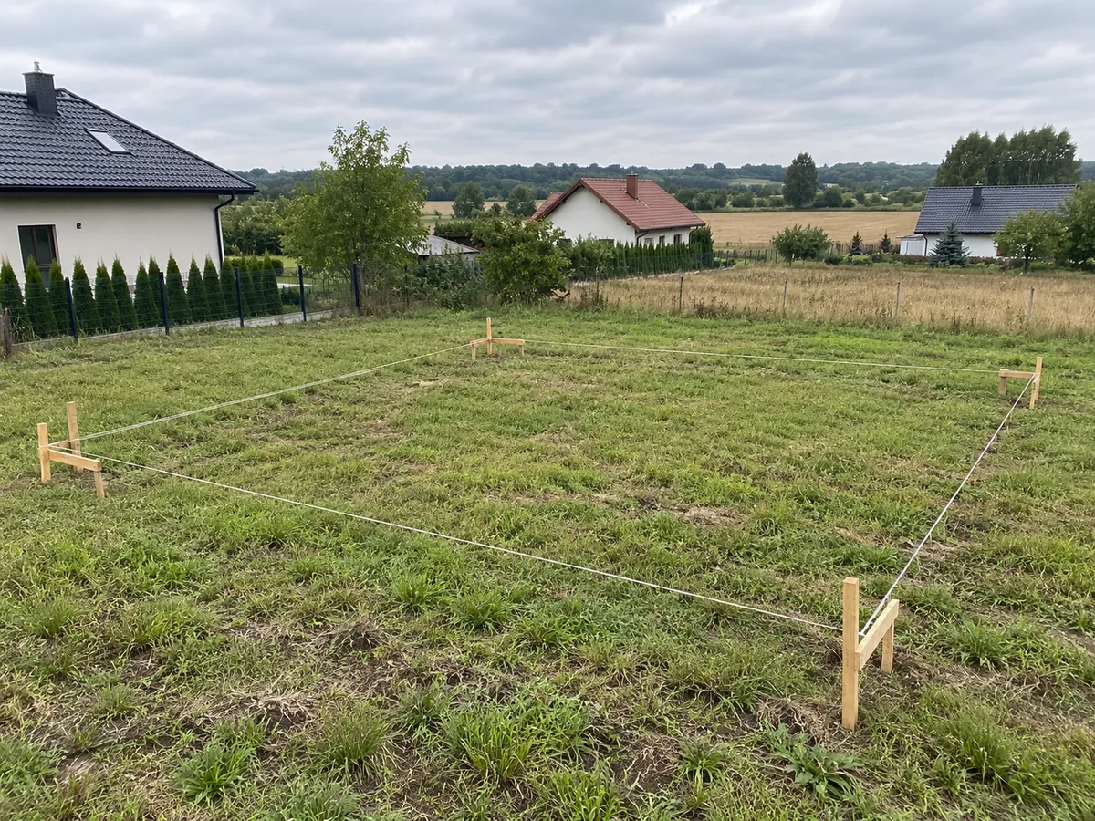 Pusta działka z trawą, paliki i sznurki wytyczające obrys domu